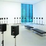 Witte museumzaal met tientallen luidsprekers en zitbanken